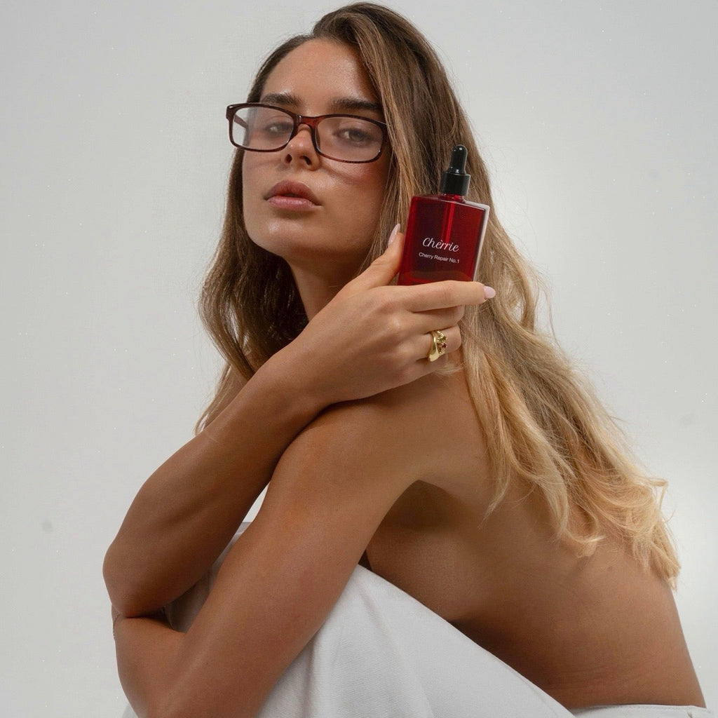 Model with long blonde wavy hair holding the Chérrie Repair No.1 hair oil bottle